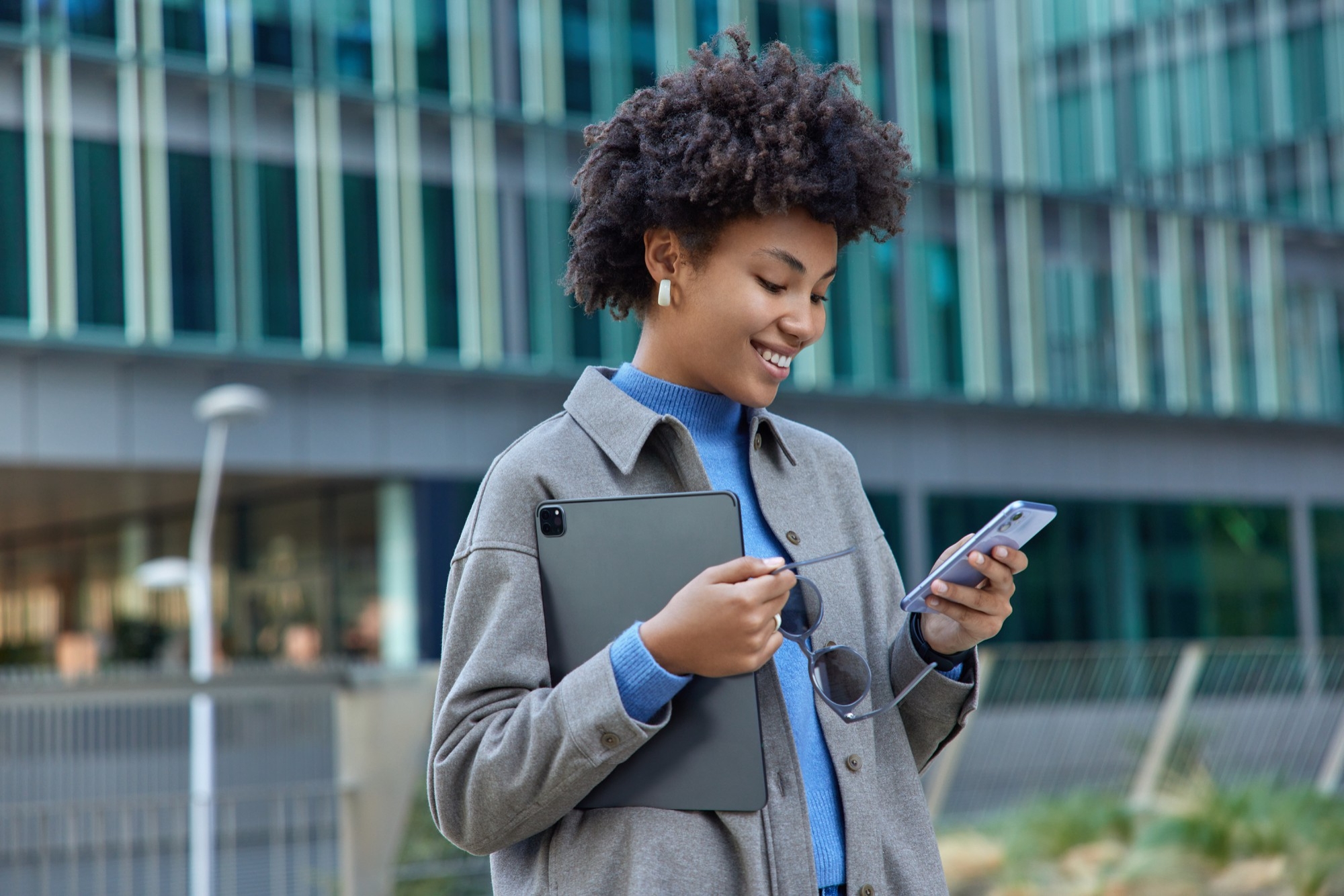 Smiling customer using PayFarGo on phone and tablet outside a modern building